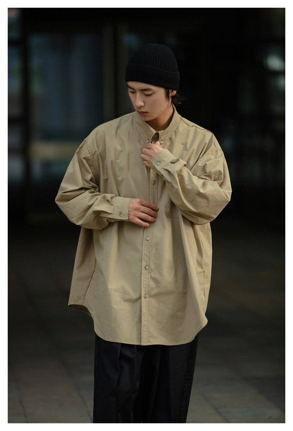 Closer front view of a model in a loose khaki button-up shirt with a chest pocket.
