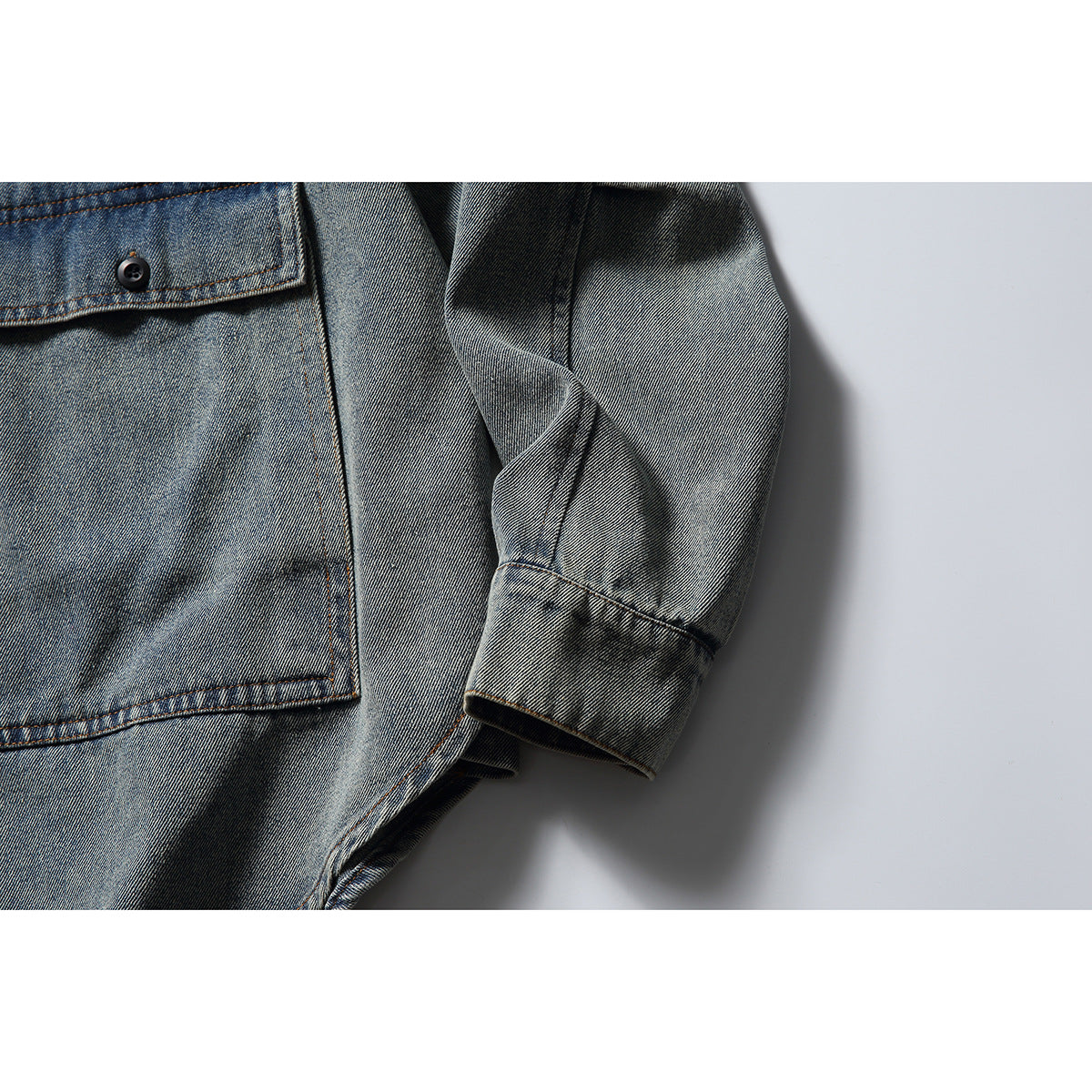 Close-up of the faded blue-gray denim jacket's sleeve, cuff, and edge of a large front pocket.