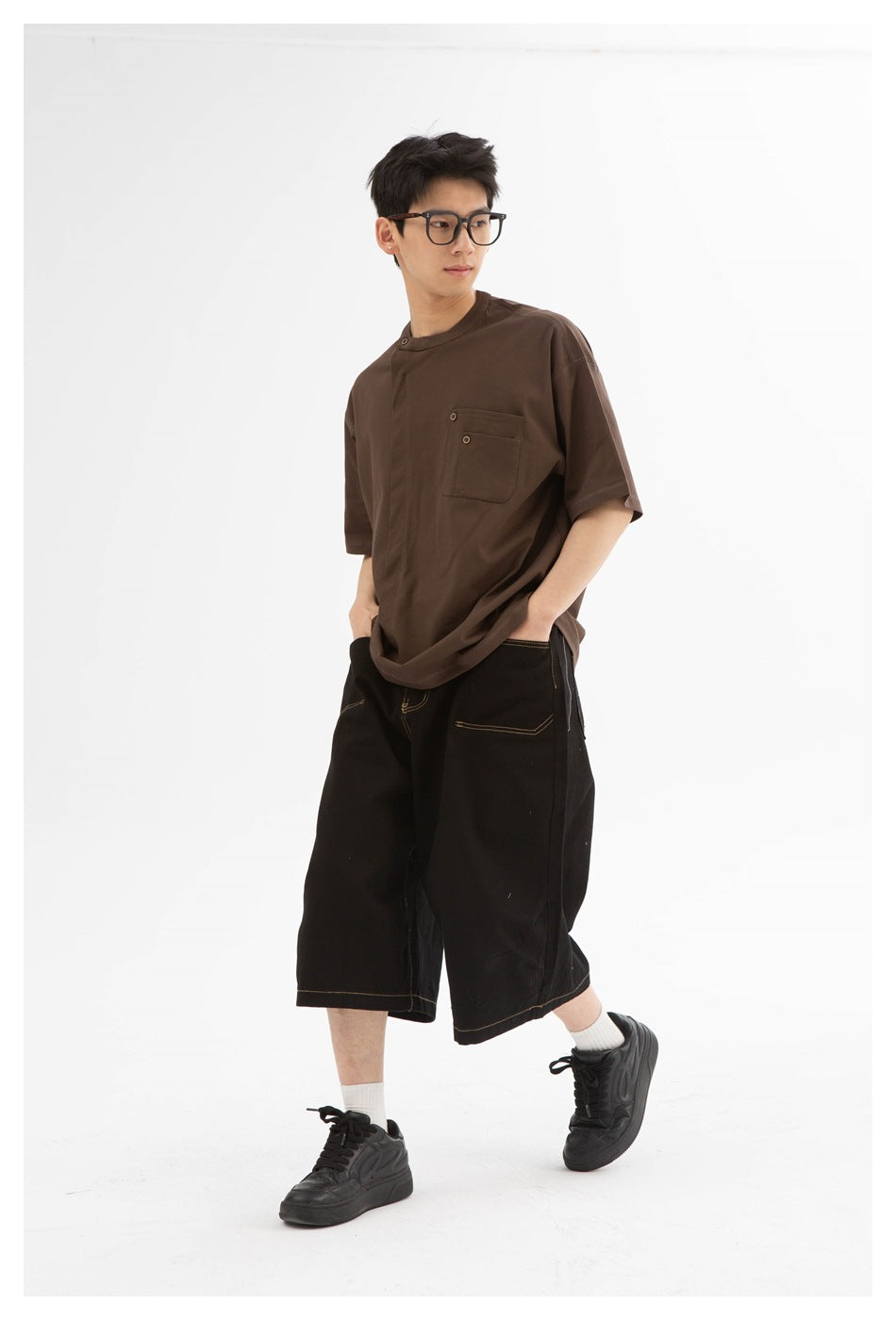 Model wearing a dark brown oversized short-sleeve T-shirt with a button-detailed chest pocket and black wide shorts.