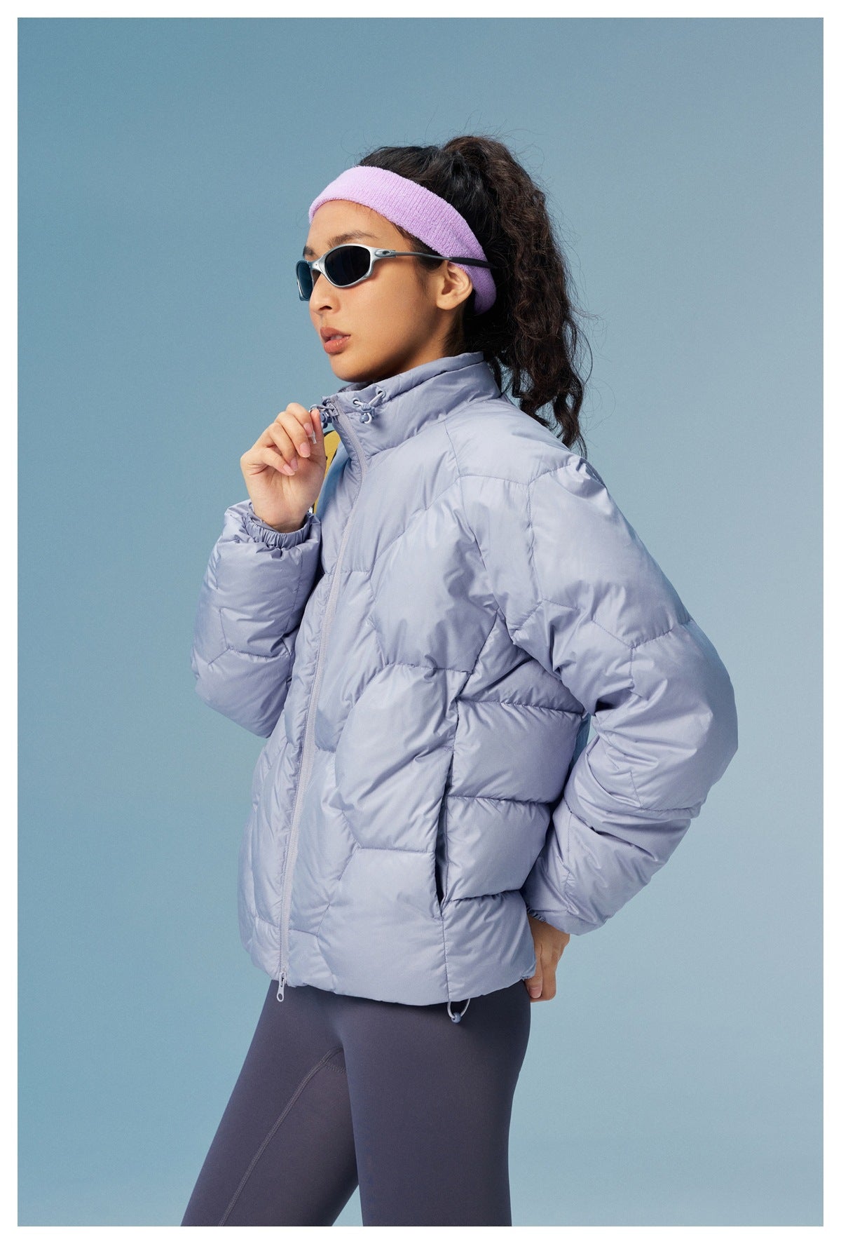 Model wearing a lavender-gray quilted jacket with a high collar, front zipper, and roomy sleeves, shown from the side.