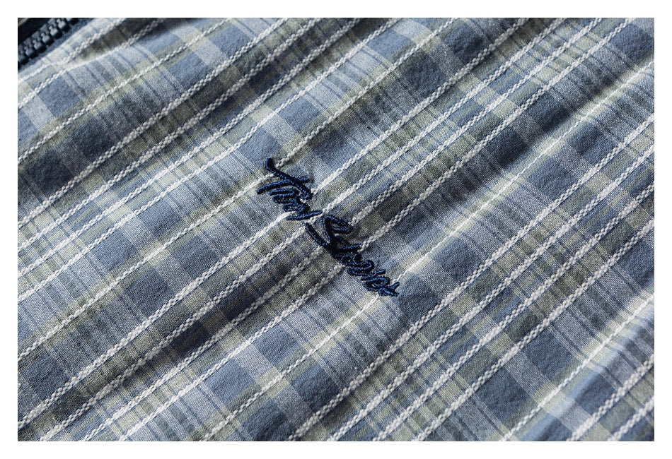 Close-up of dark embroidered script on blue-gray plaid shirt fabric.