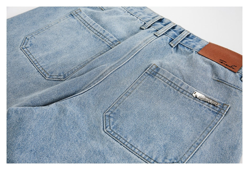 Close view of the upper back of light blue jeans, showing two pockets, belt loops, and a leather waistband patch.