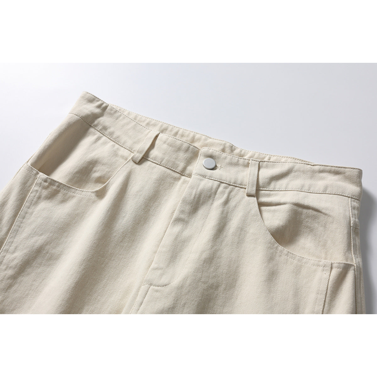 Close-up of ivory wide-leg trousers showing the waistband, button, belt loops, and curved front pockets.