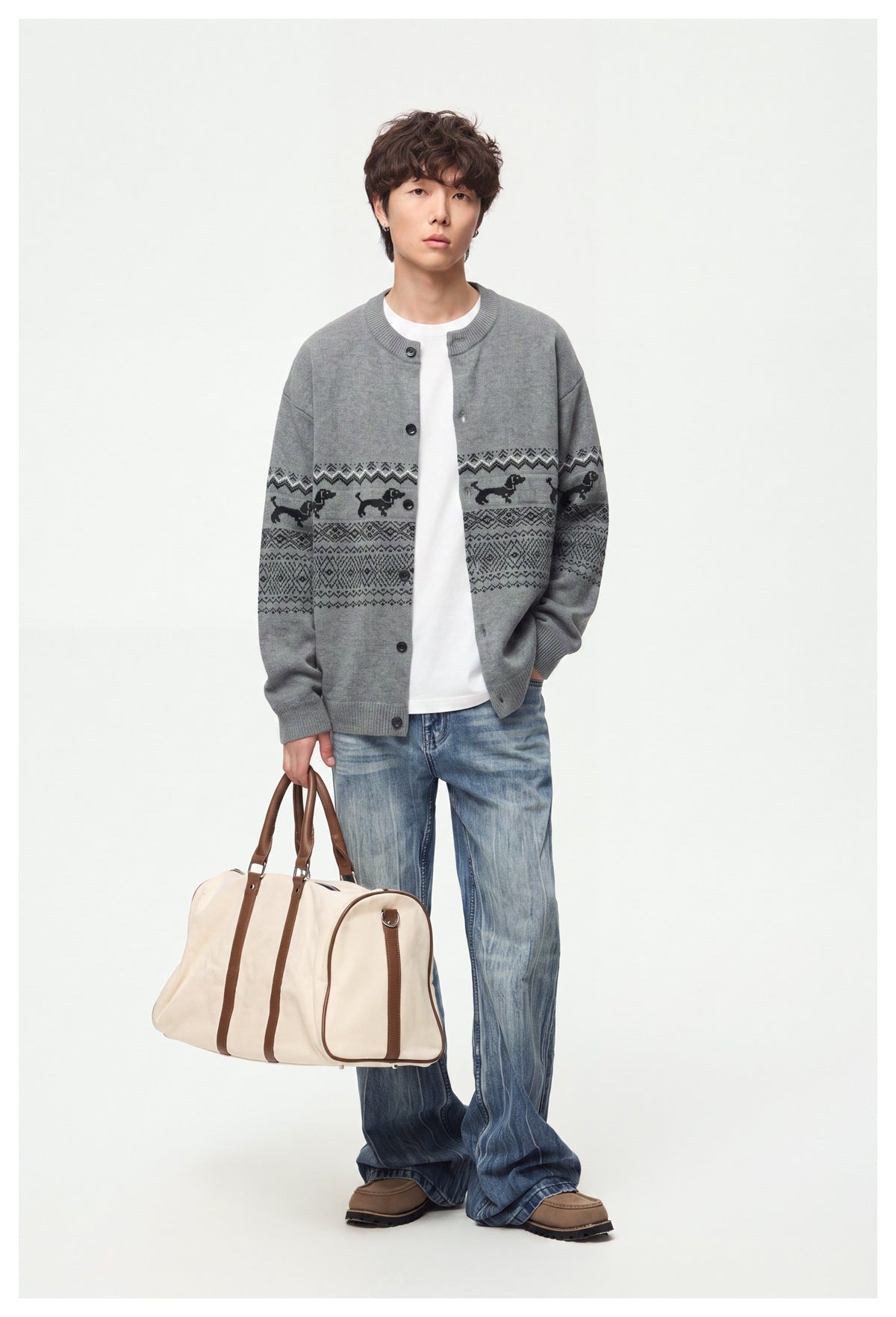 Model wearing a gray button-front cardigan with black geometric bands and dog motifs, jeans, and carrying a large bag.