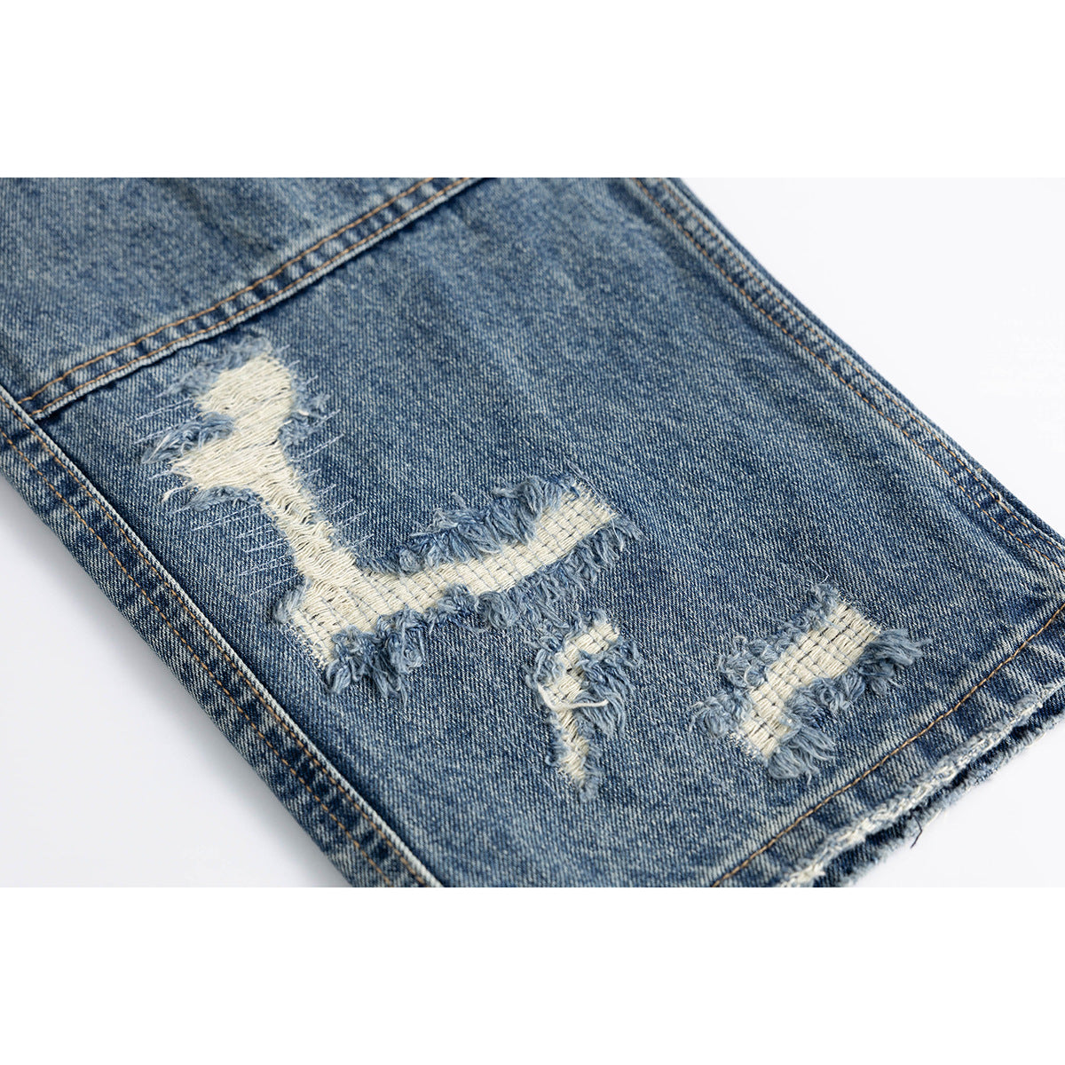 Close-up of a blue denim leg with several frayed distressed openings and a raw hem.