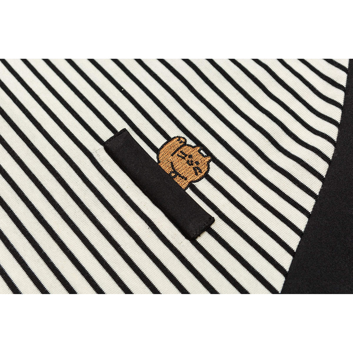 Close-up of a small orange embroidered character beside a black fabric tab on cream-and-black stripes.