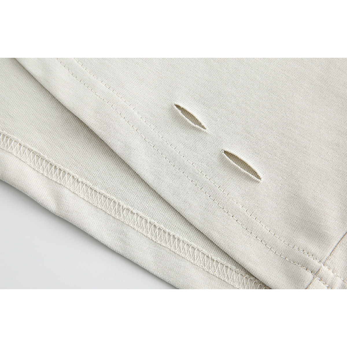 Close-up of cream fabric showing two small slits, parallel stitching and an overlocked seam.