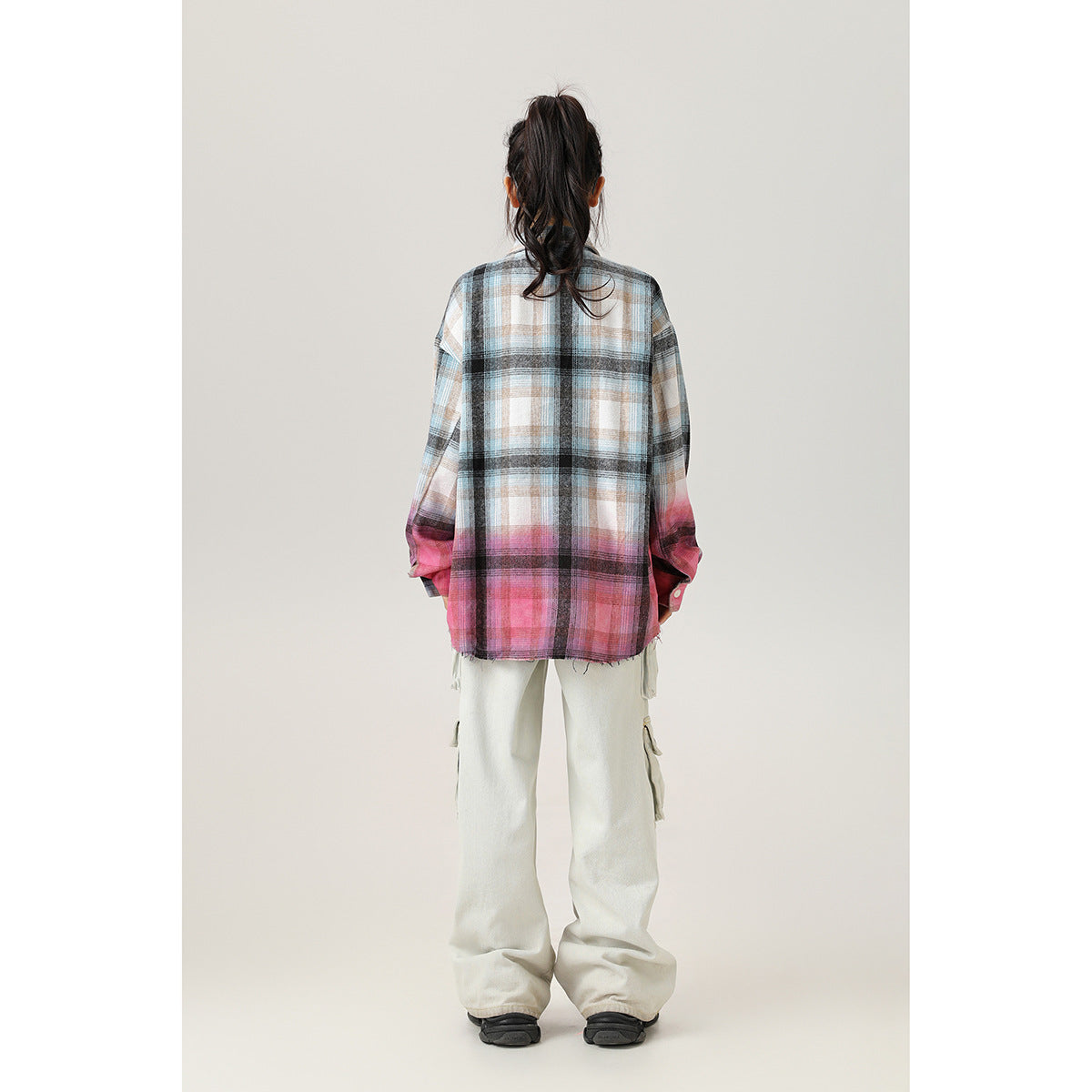 Back view of a model wearing an oversized plaid shirt with pink lower panels and light cargo pants.