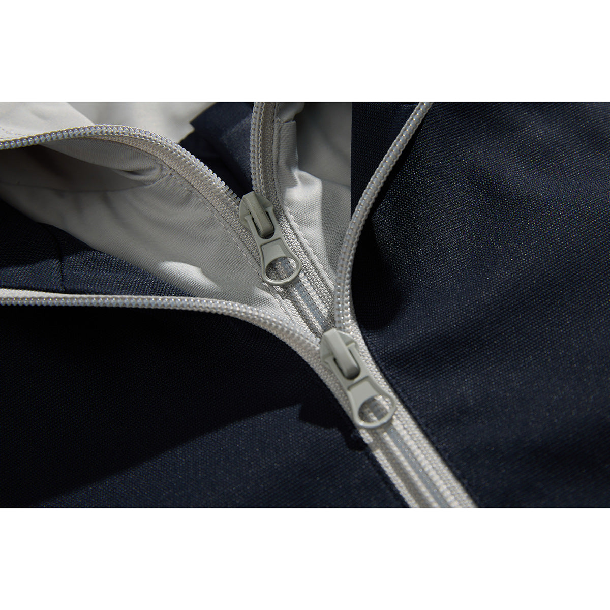 Close-up of two light gray zipper pulls and contrasting trim on a navy jacket.