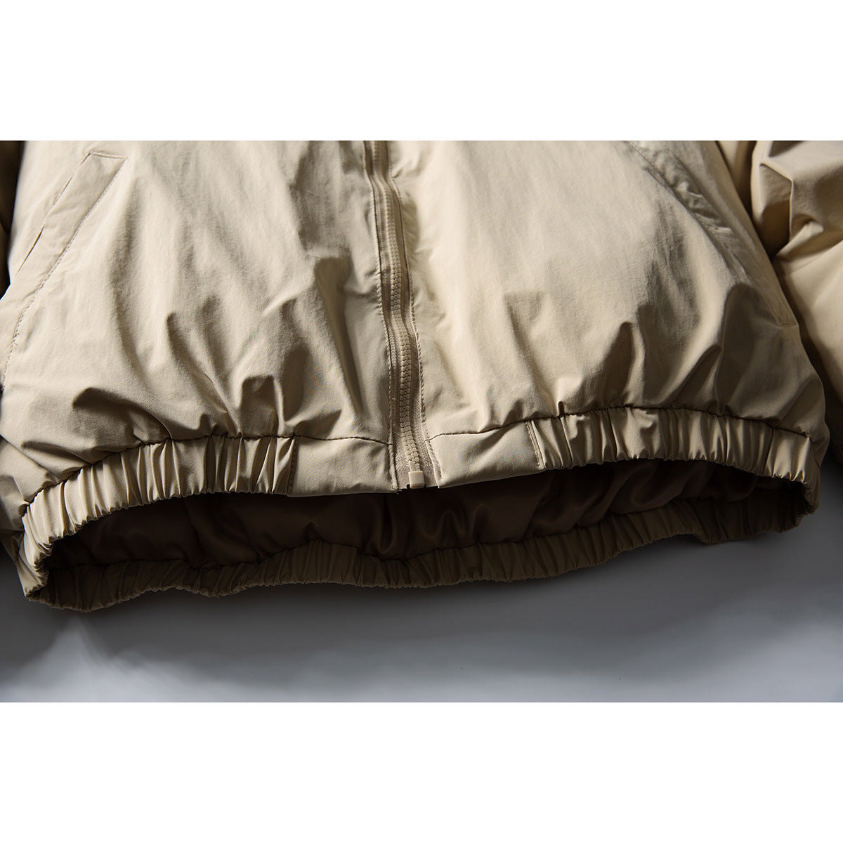 Close-up of a light beige jacket’s center zipper and gathered elastic hem.