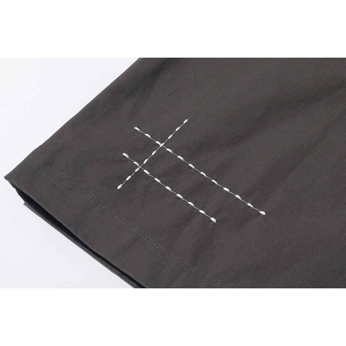Close-up of white decorative cross-stitching on the hem of a charcoal jacket.