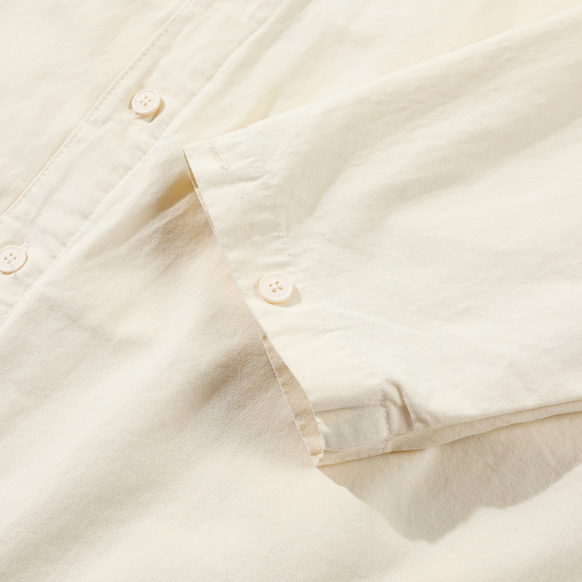 Close-up of an ivory shirt sleeve, cuff, and white buttons.