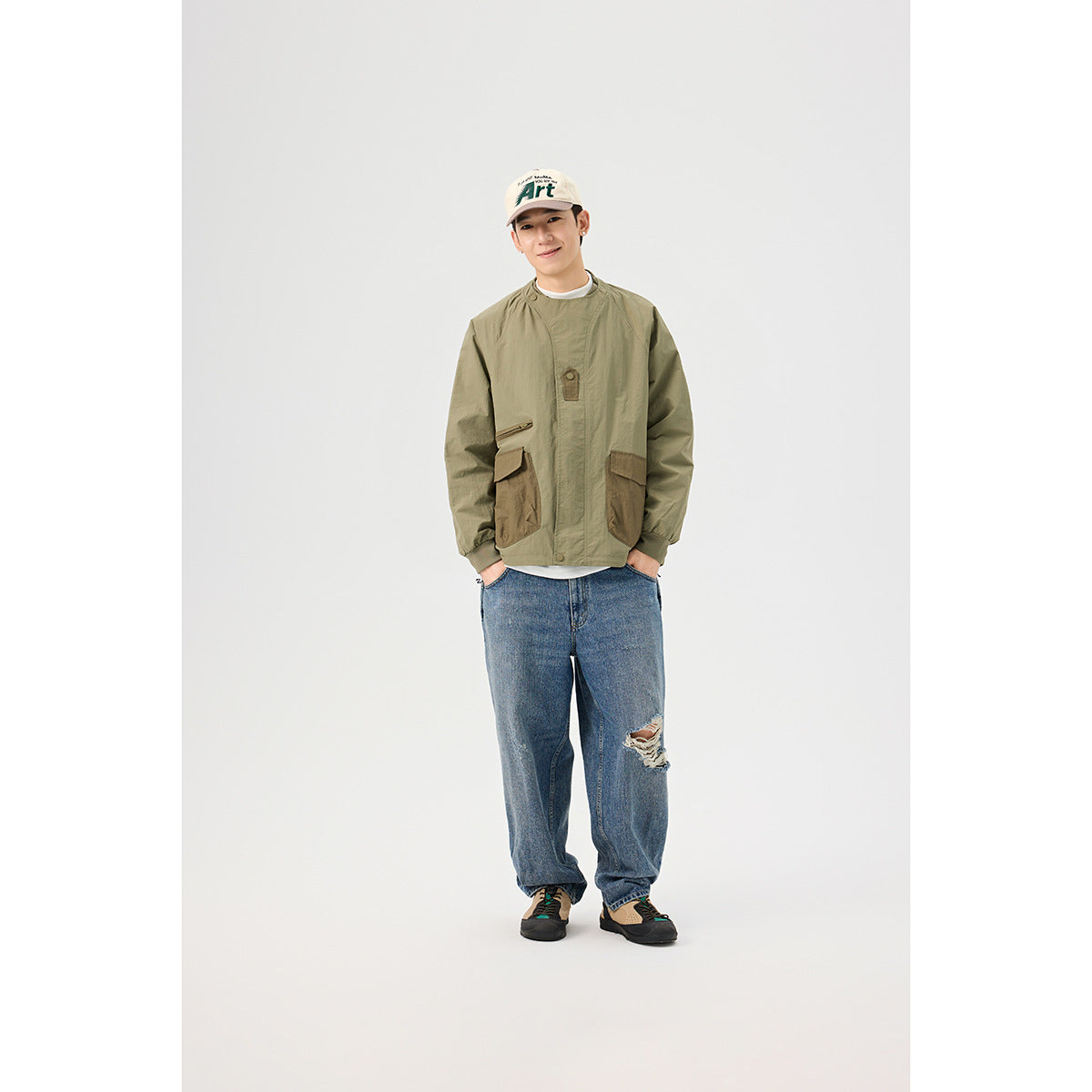 Model wearing an olive jacket with brown utility pockets, blue jeans, and a cream cap, shown from the front.