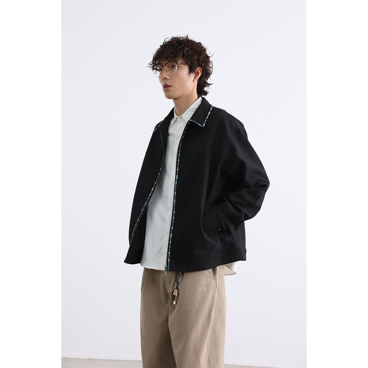 Model wearing a loose black zip-front jacket with multicolor trim over a white shirt, shown at an angle.