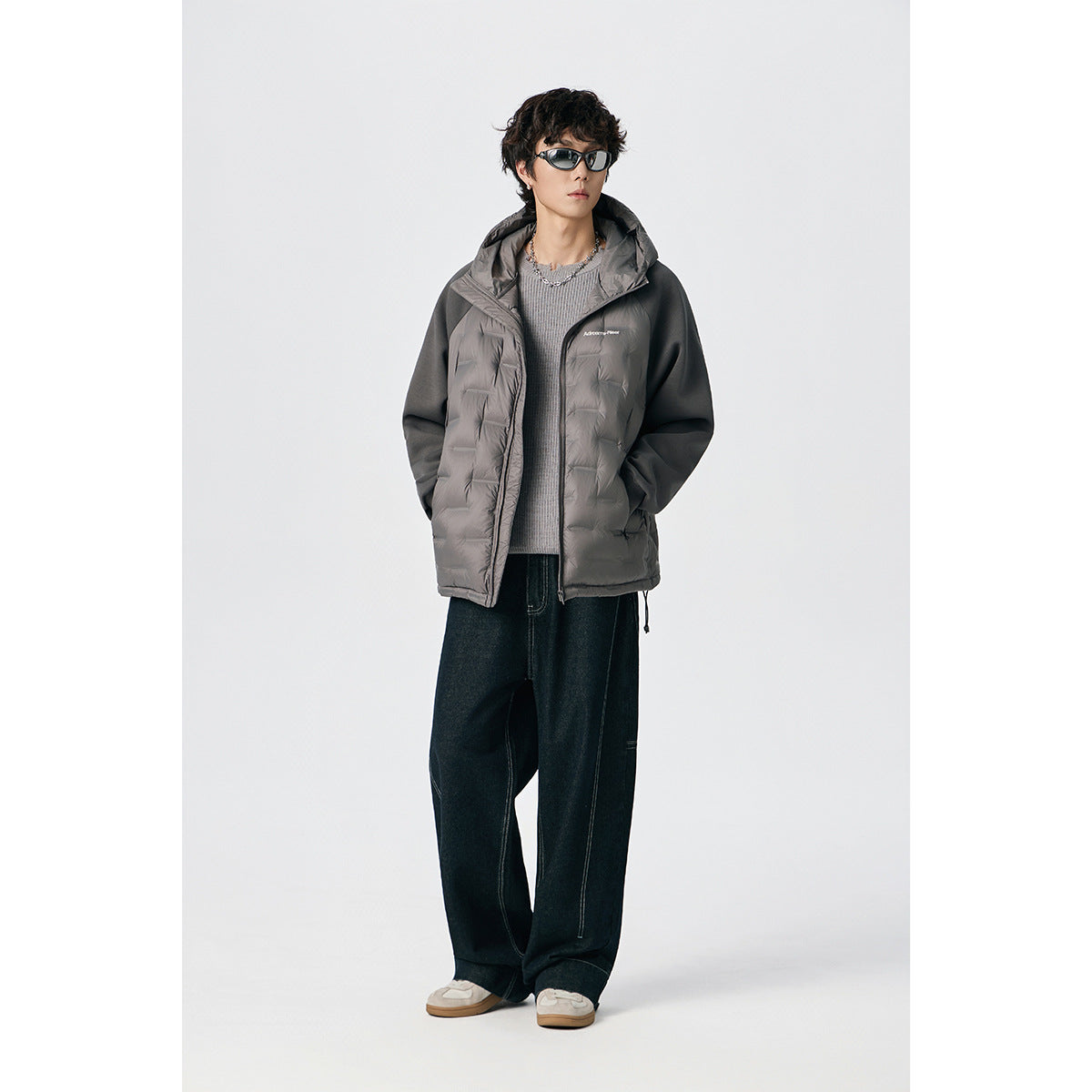 Model wearing a gray hooded jacket with quilted front panels, dark sleeves, and a front zipper.
