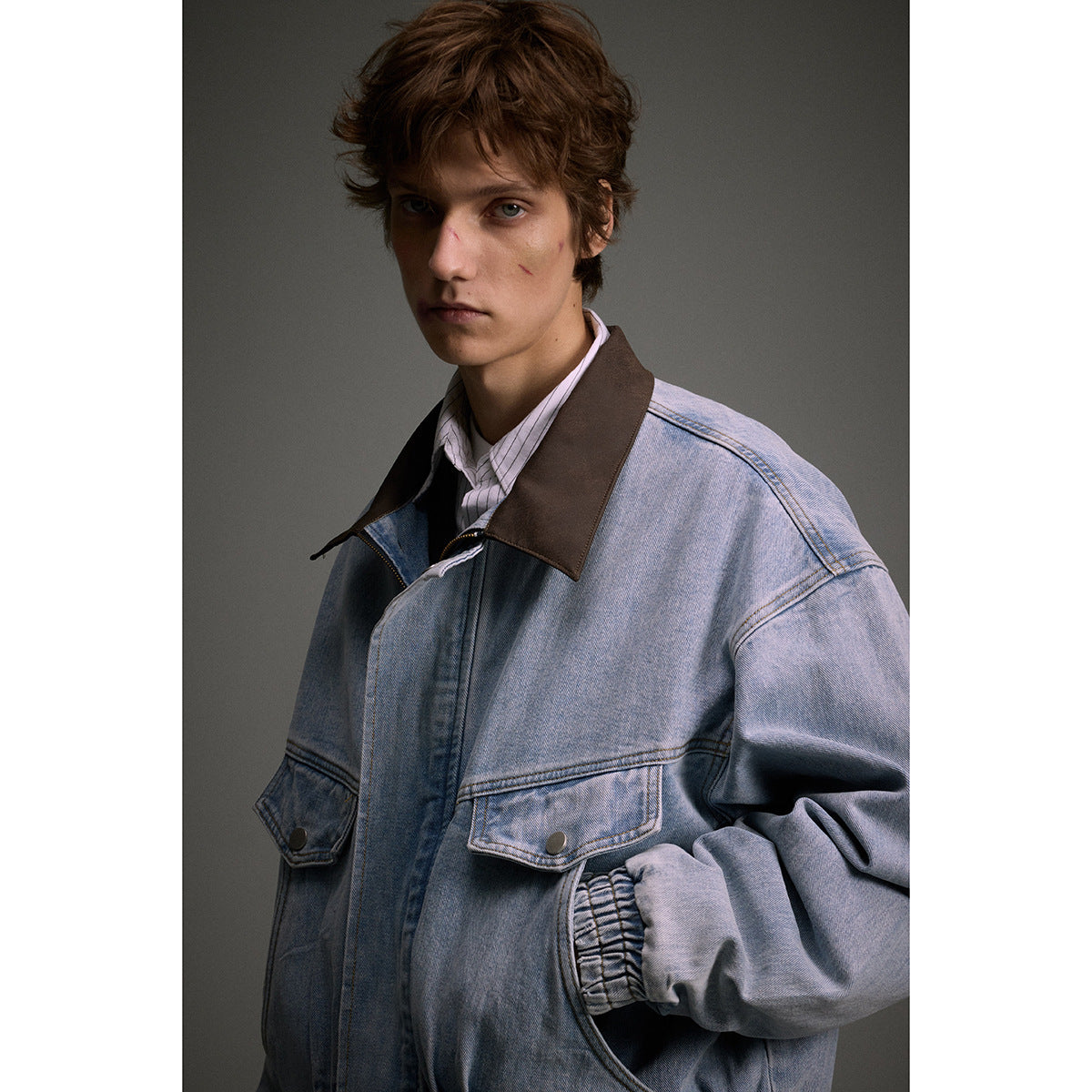 Close-up of a model wearing a light blue denim jacket with a brown collar and buttoned flap pockets.