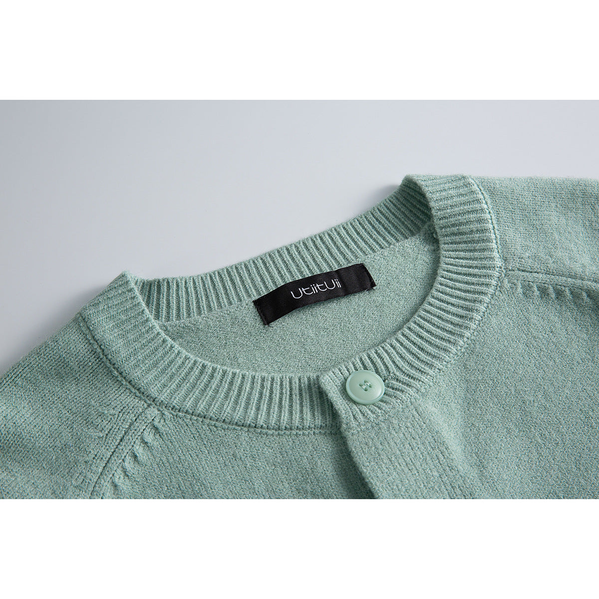 Close-up of a pale mint-green knit cardigan collar, button, and sewn-in neck label.