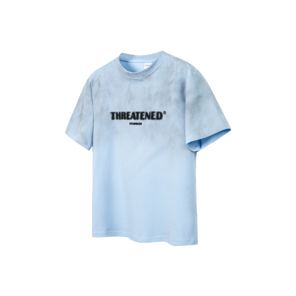 Pale blue short-sleeve crew-neck T-shirt with a centered black chest logo and subtle mottled shading.