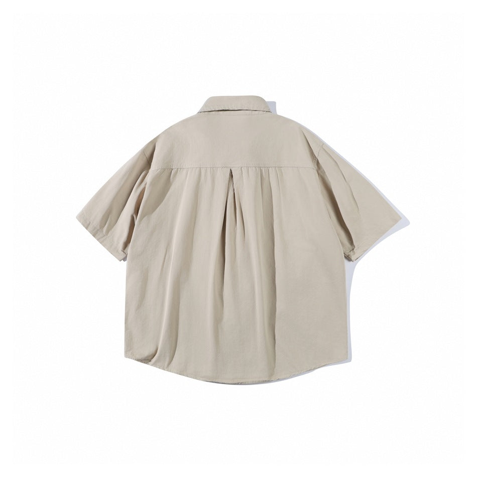 Back view of a light beige short-sleeve button-up shirt with a yoke and center pleat, laid flat.