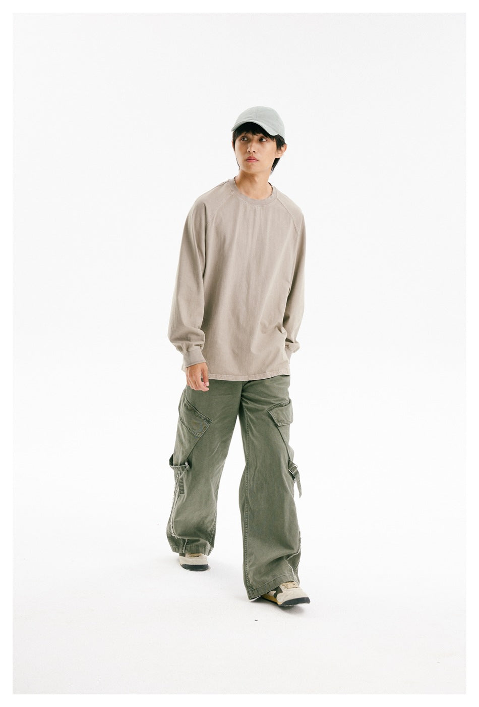 Model in a loose taupe crewneck and olive cargo pants, shown walking in a three-quarter view.