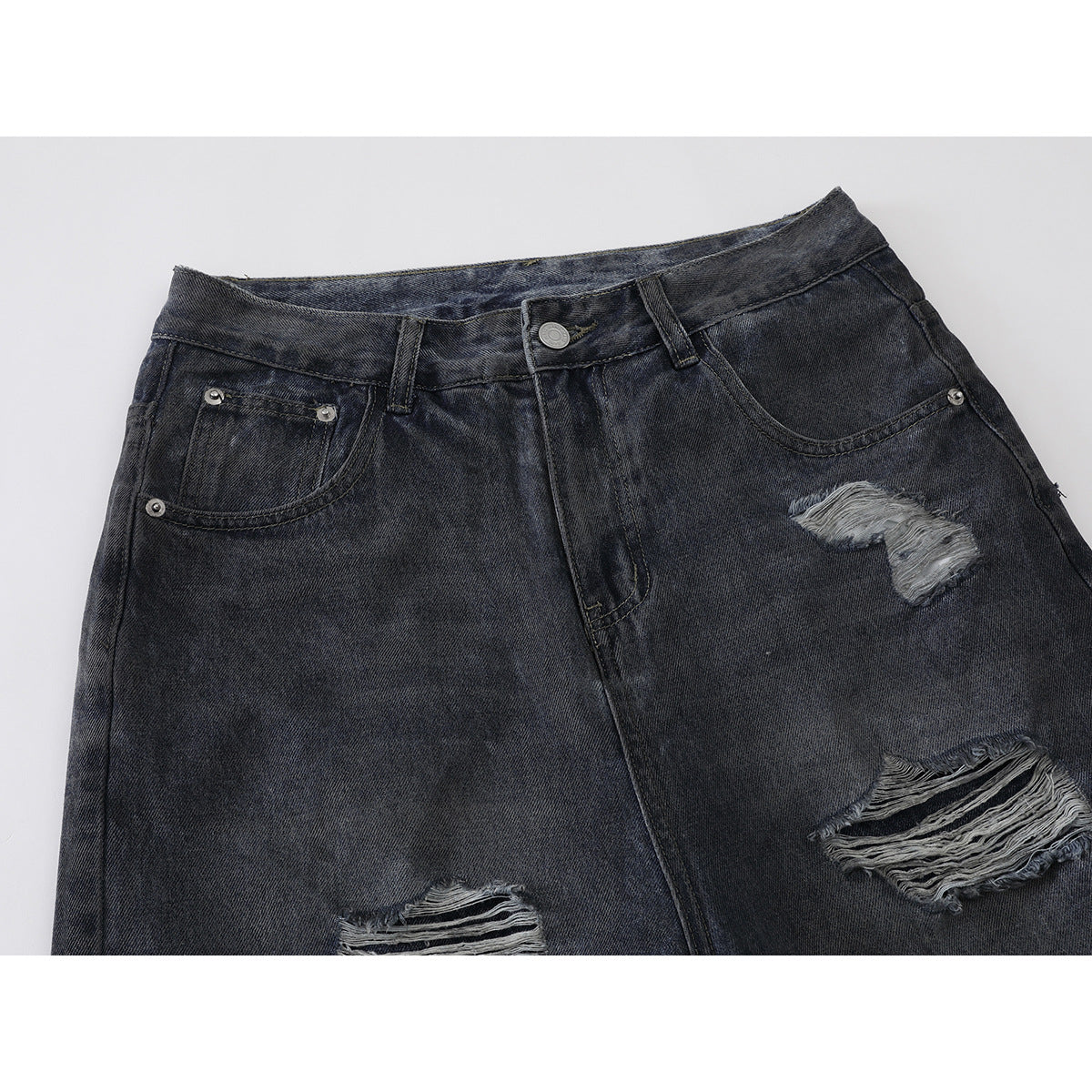 Close-up of the front waistband and pockets of charcoal distressed jeans with several frayed rips.