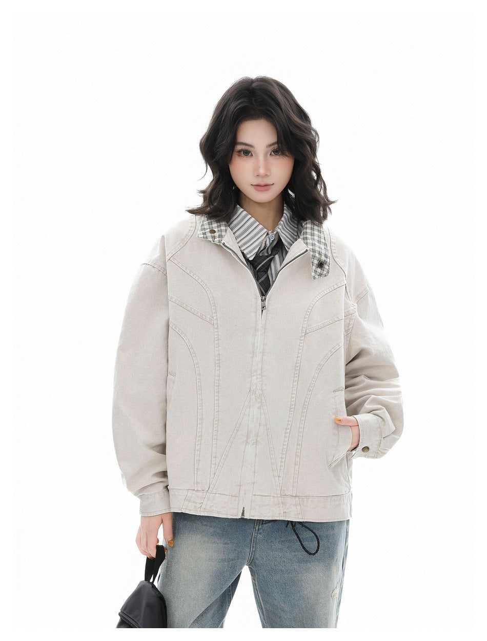 Model wearing a light beige zip-front jacket with curved seams and a plaid-lined stand collar, over a striped shirt.