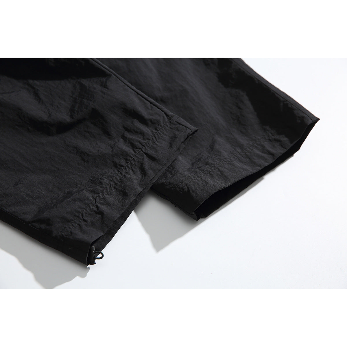Close-up of black trouser legs and hems, showing the fabric and a small adjustable hem loop.