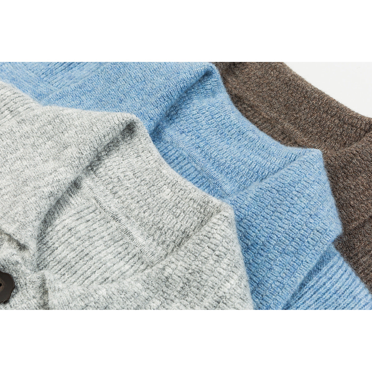 Close-up of overlapping gray, blue, and brown knit cardigans showing textured fabric and ribbed edges.