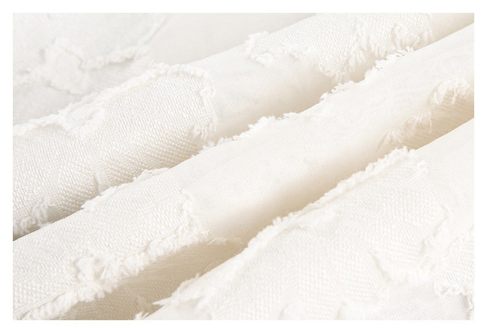 Macro view of ivory fabric showing raised floral texture and overlapping folds.