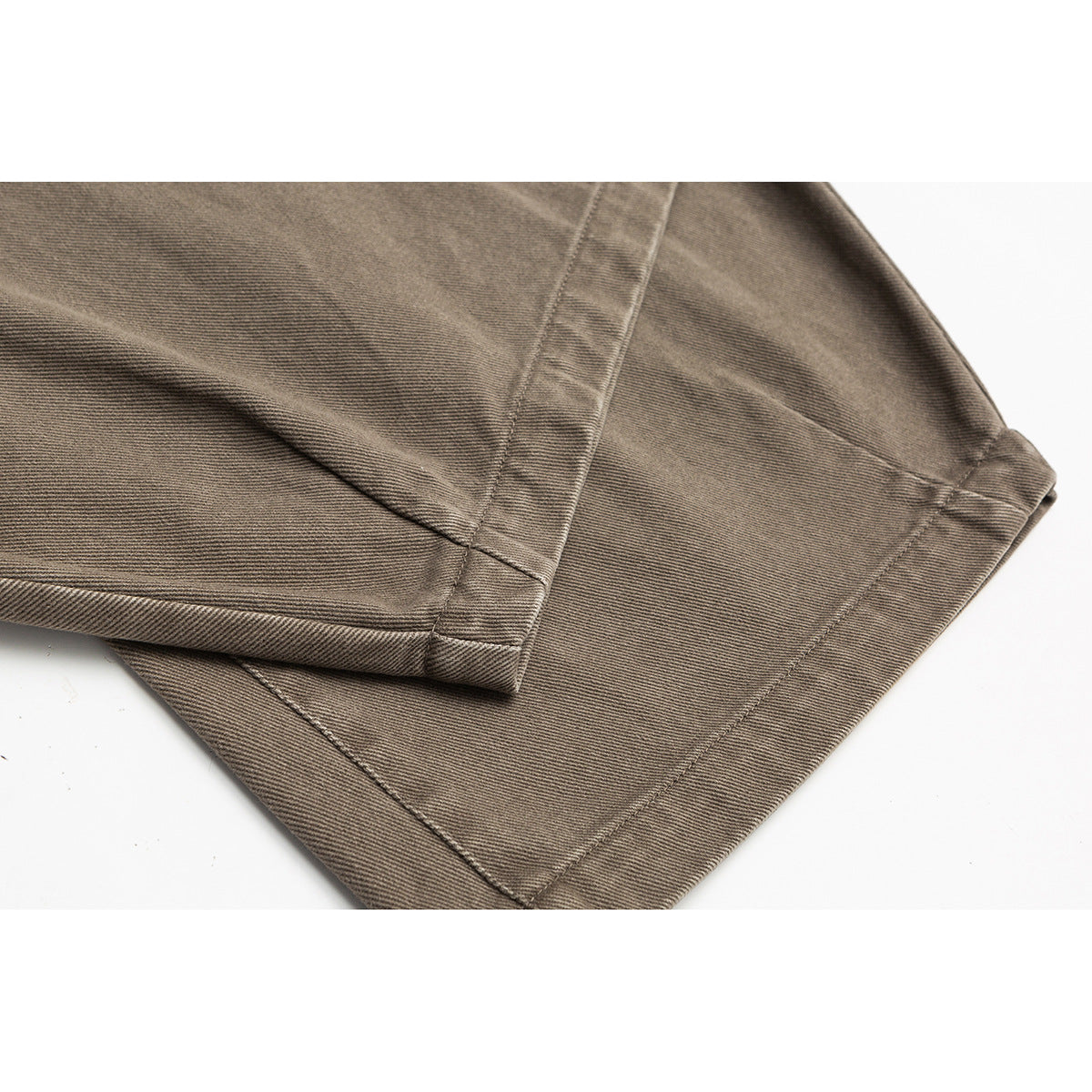 Close-up of the stitched hem and folded leg of taupe trousers.