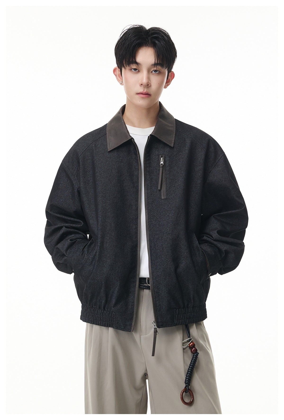 Close front view of a model in a black-gray zip jacket with brown collar, hands in pockets, over a white tee