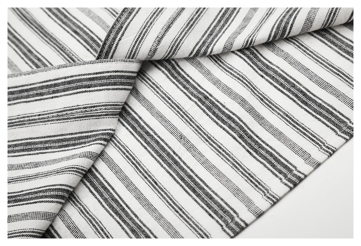 Close-up of white fabric with narrow black woven stripes, draped in overlapping folds.
