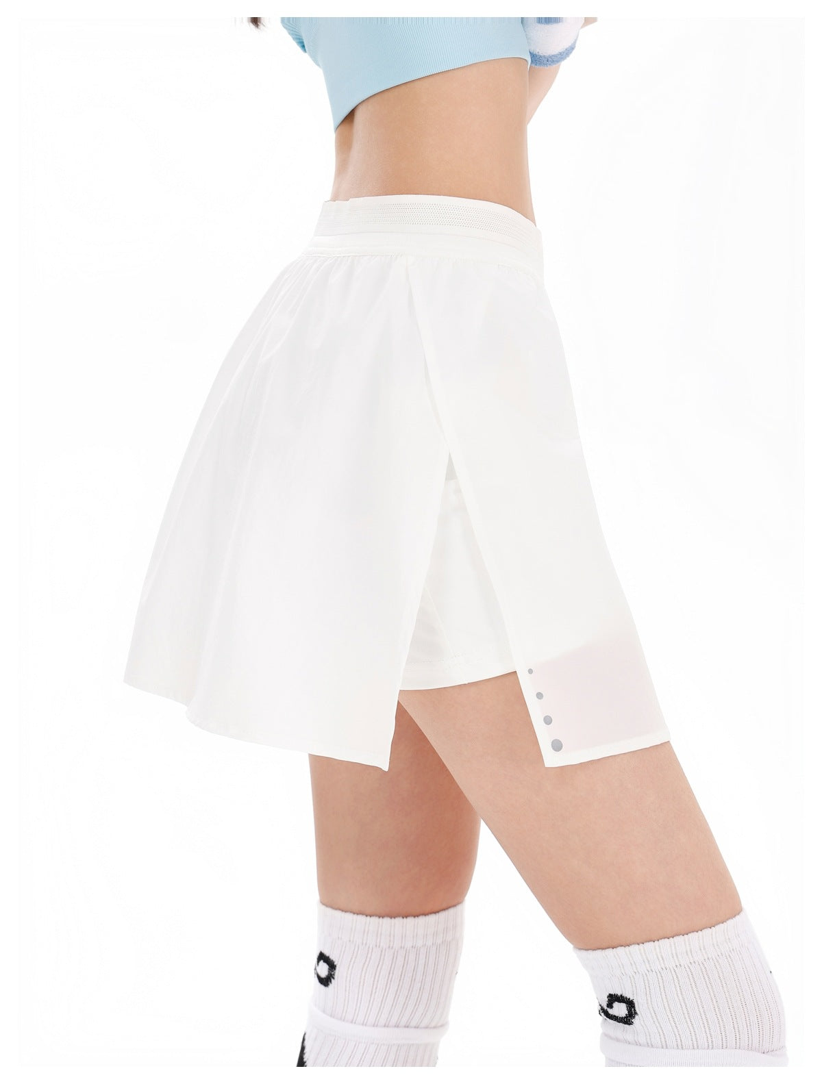 Cropped model wearing a white wrap-panel athletic skirt over shorts, with a wide waistband and small gray dots near the hem.