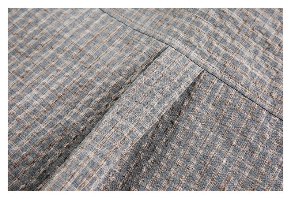 Close-up of a stitched patch pocket on gray-brown plaid shirt fabric.