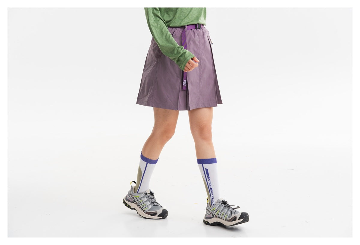 Cropped model wearing a muted mauve pleated skirt with a purple belt, shown from the front with a green top.