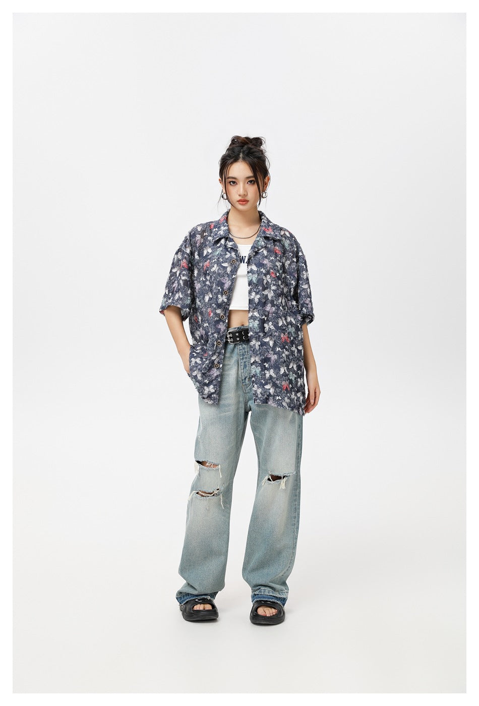 Front view of a model in an oversized navy butterfly-print shirt, white crop top and ripped light-wash jeans.