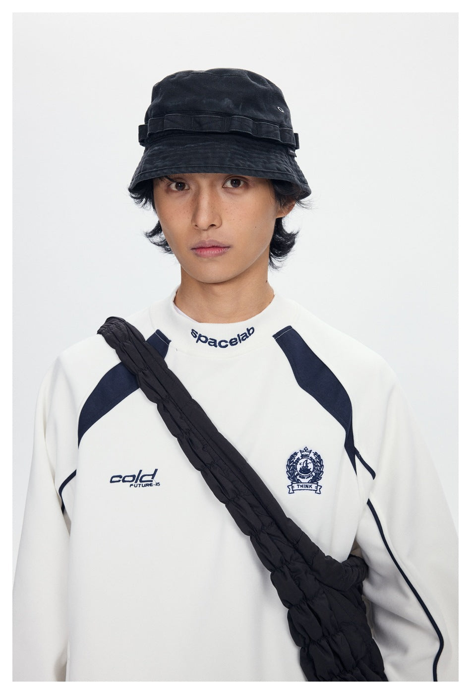 Close view of a model wearing a white sweatshirt with navy panels and embroidered chest graphics.