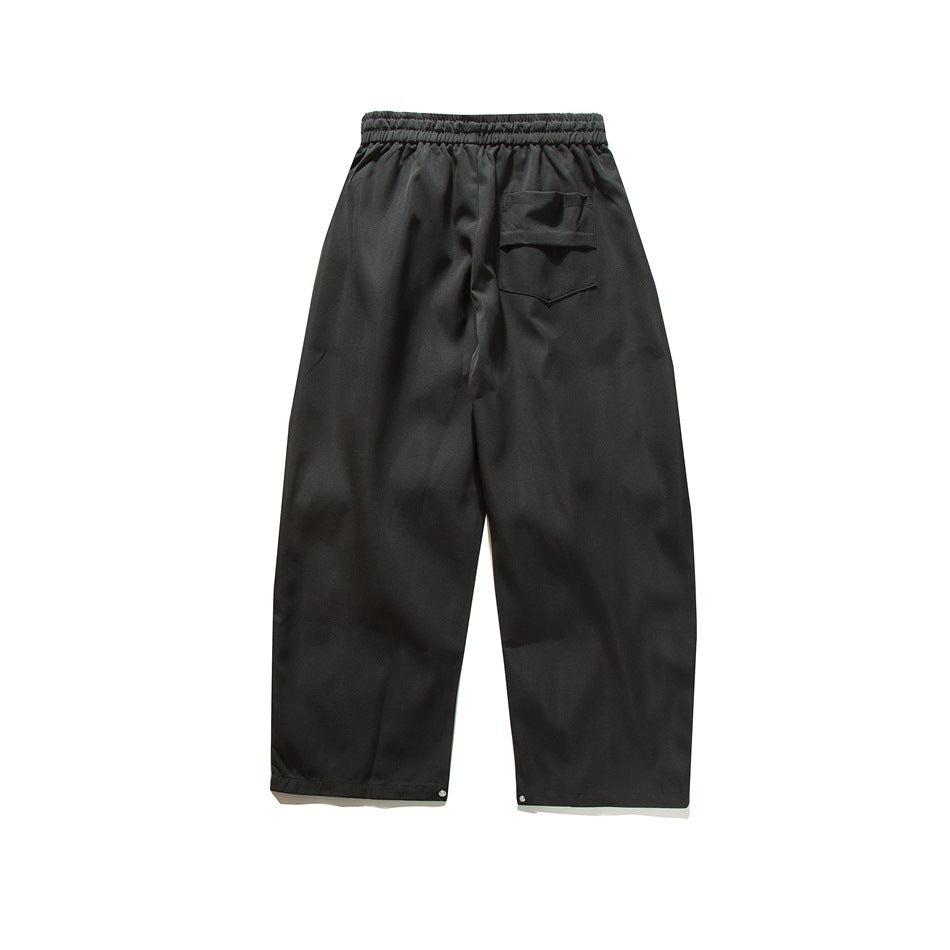 Back view of black wide-leg pants with an elastic waistband, rear patch pocket, and snap-adjustable hems.