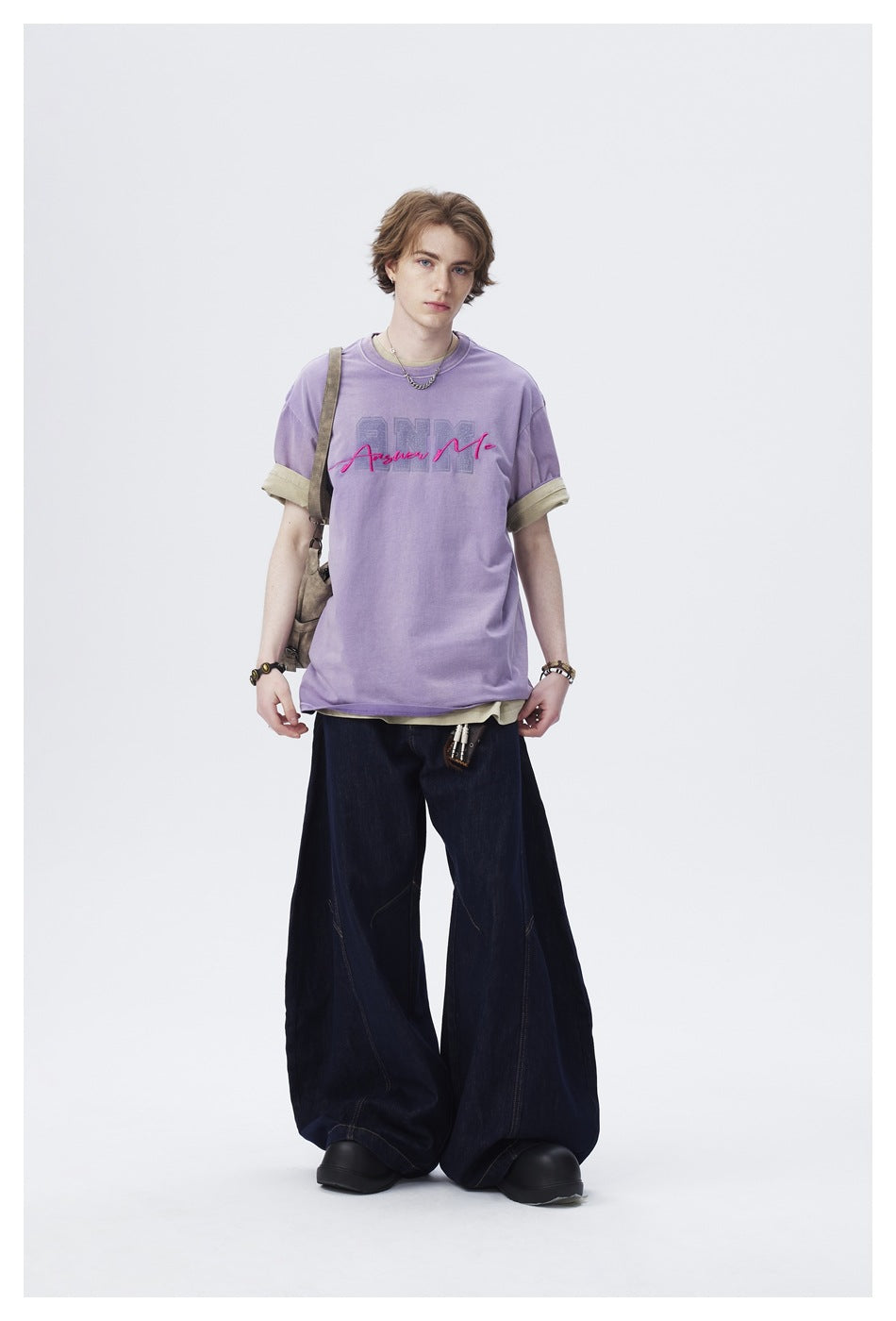 Model wearing a lavender graphic T-shirt with rolled sleeves and very wide dark jeans, shown full length.
