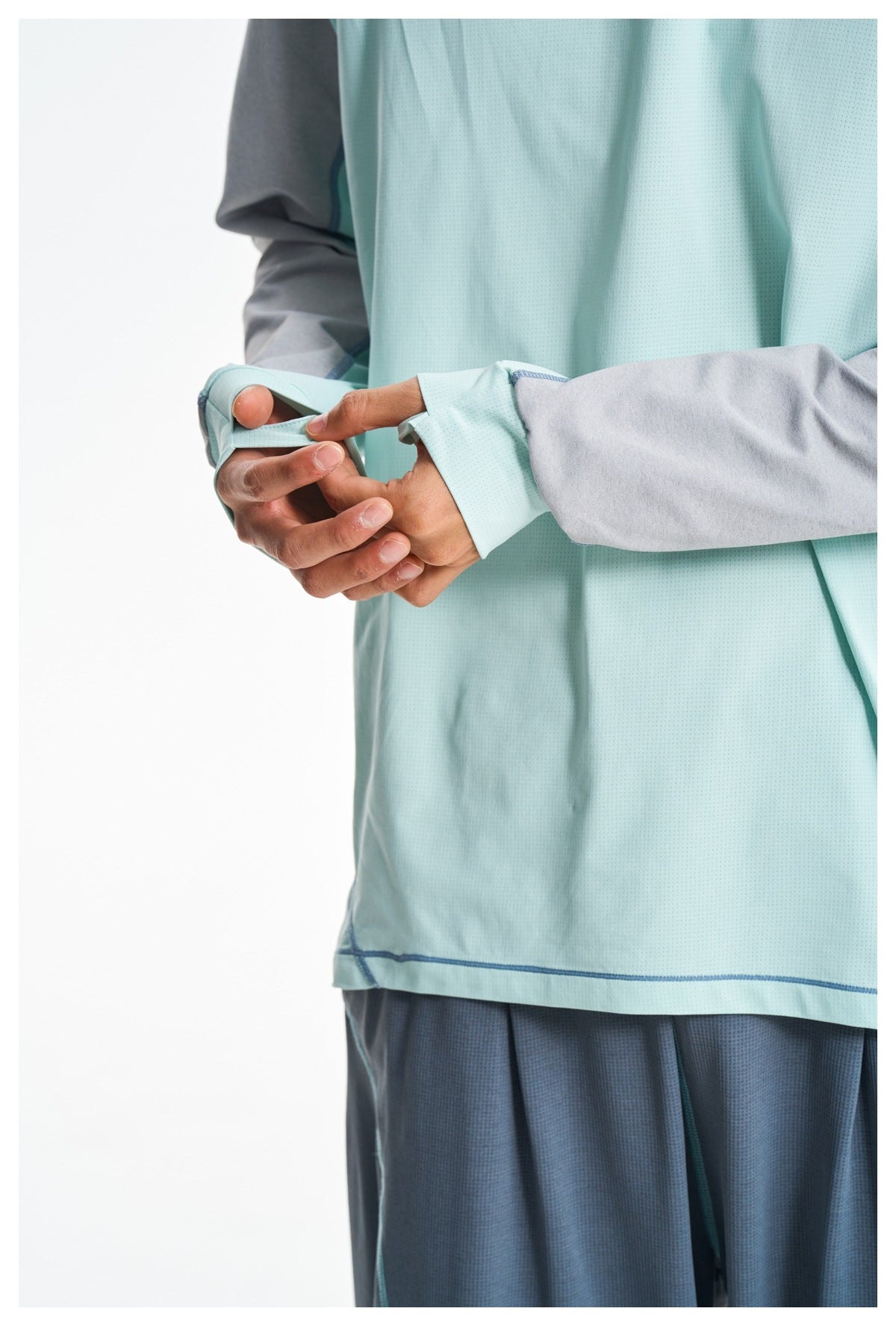 Close-up shows the mint-green shirt's sleeve cuff with a thumb loop, gray sleeve panel, and blue seam stitching.
