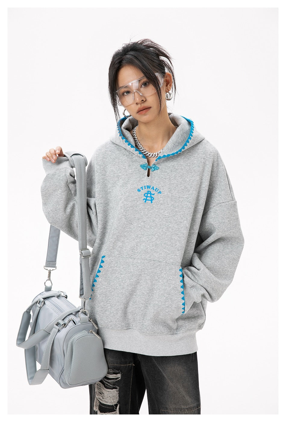 Model wearing an oversized heather-gray hoodie with bright blue trim, chest emblem, kangaroo pocket and toggle closure.