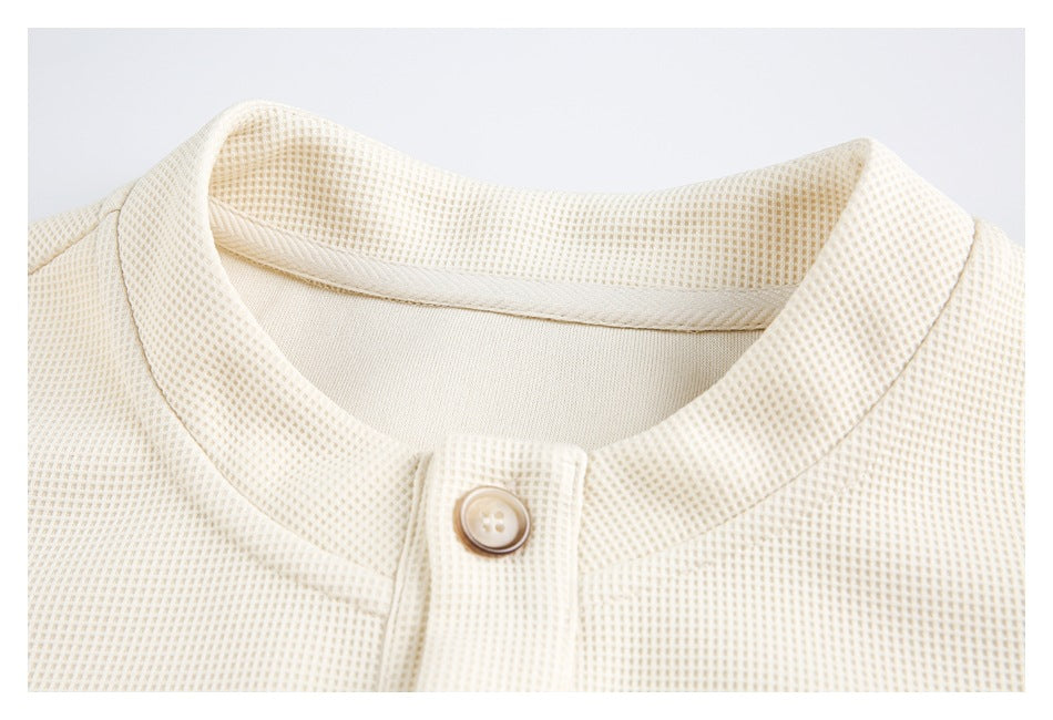 Close-up of the cream knit top's rounded neckline and single-button front placket.