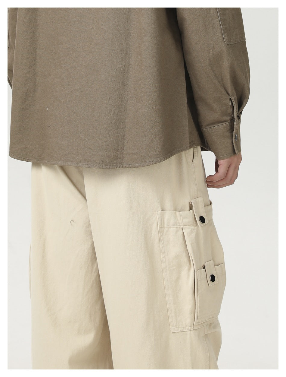 Close-up of cream cargo pants showing a large side pocket with two snap-button flap tabs.