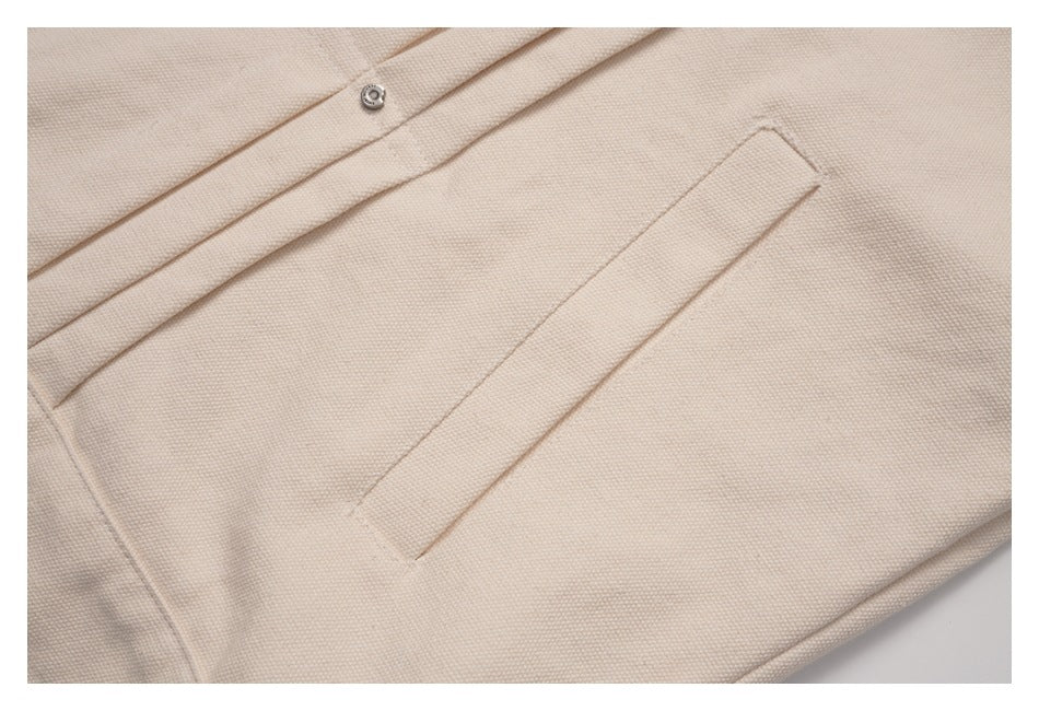 Close-up of a slanted welt pocket and snap-fastened placket on a beige jacket.