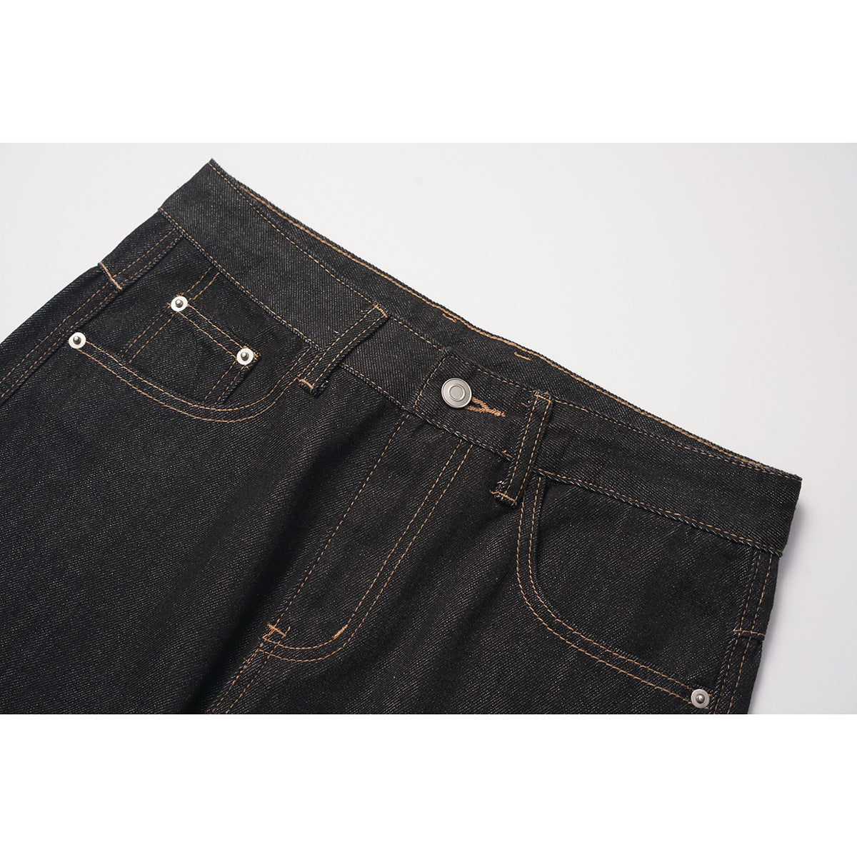 Close-up of black jeans showing the front waistband, button, pockets, rivets, and contrast stitching.