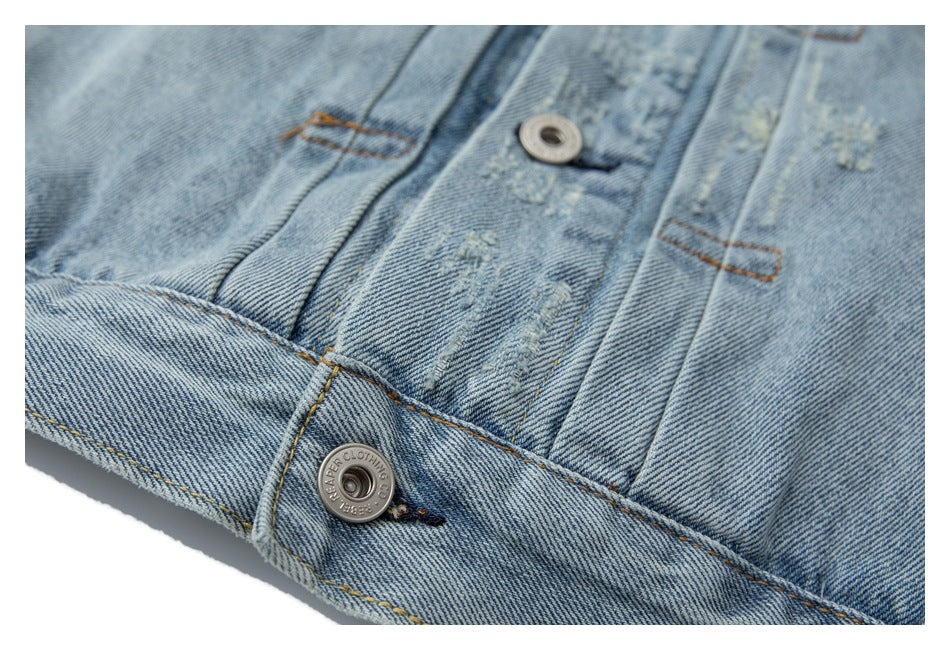 Close-up of a light-wash denim jacket front with distressed marks, button, and orange topstitching.