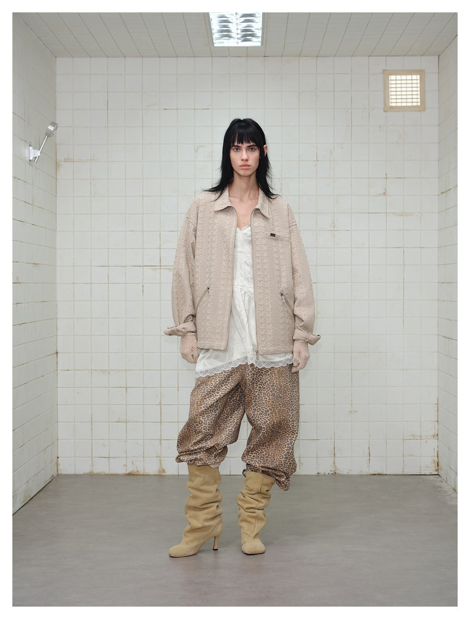 Person wearing a beige textured zip jacket with a collar, white lace-trim top, leopard-print pants and tan boots.