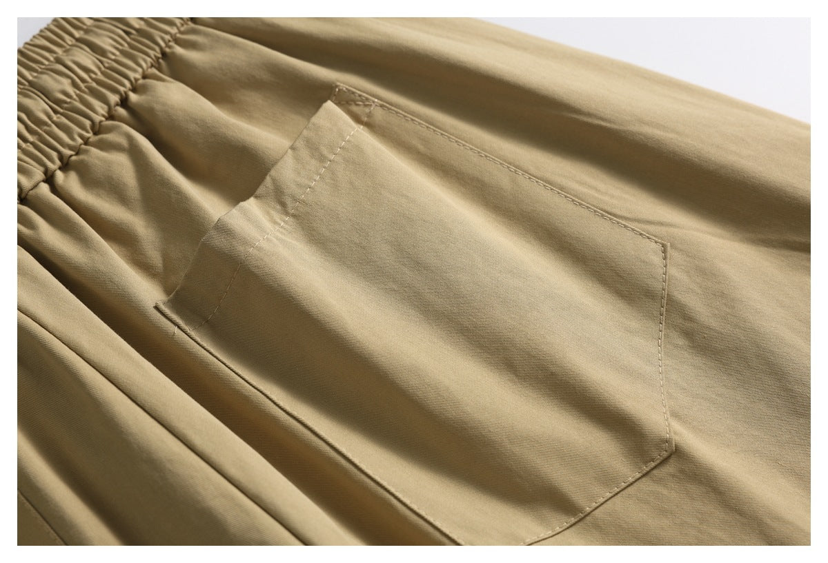 Close-up of tan shorts showing a large stitched patch pocket below the gathered waistband.