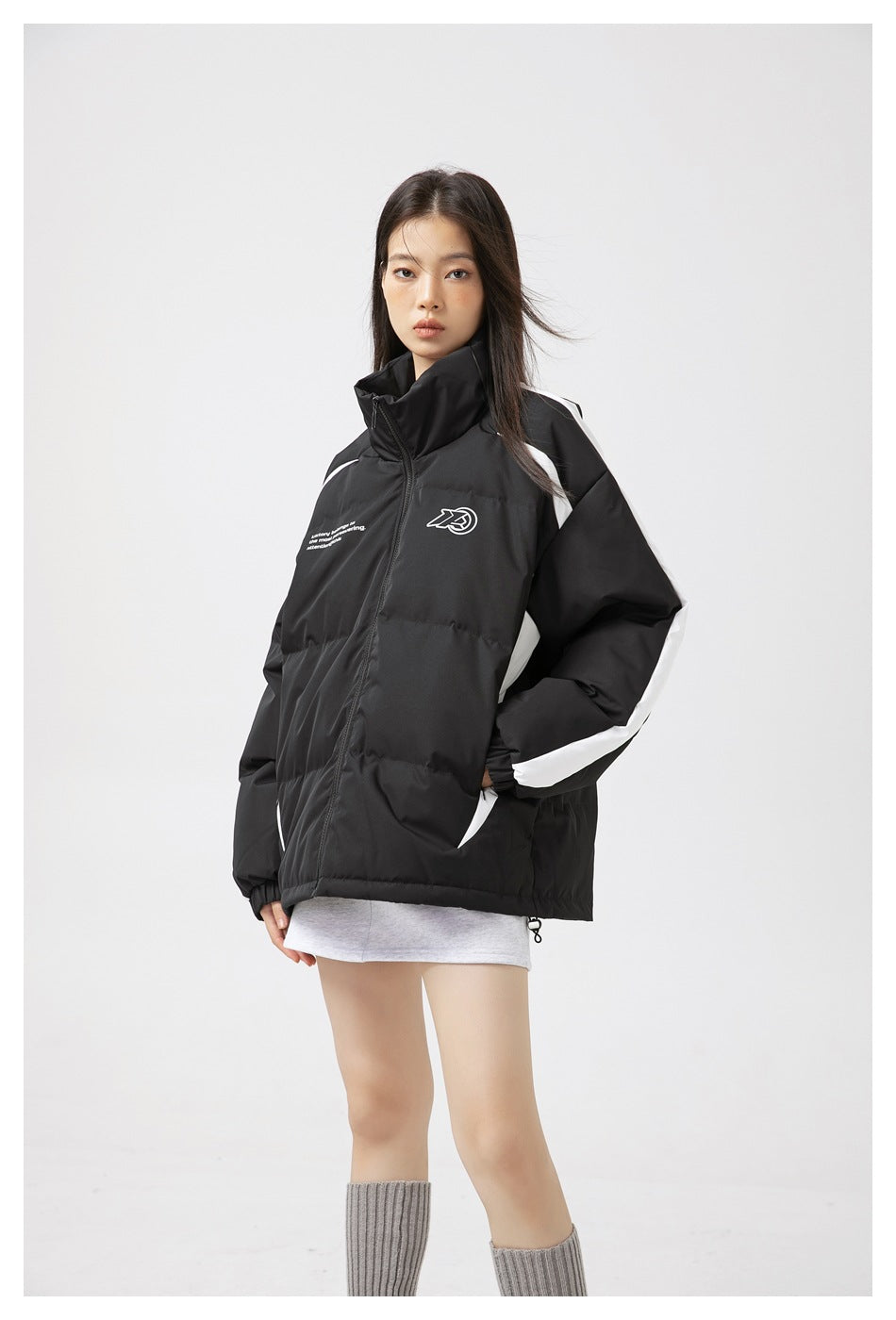 Front view of a model wearing a black padded jacket with a high collar, white side and sleeve stripes, and chest graphics.