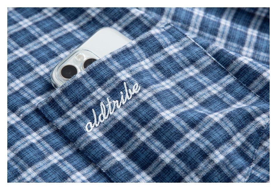 Close-up of a blue-and-white plaid shirt pocket with white script embroidery and a phone tucked inside.